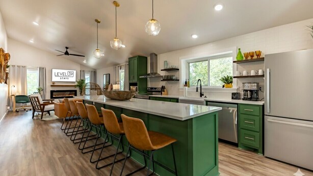 Een moderne keuken met groene kastjes, een groot kookeiland met barkrukken en hanglampen.