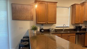 A kitchen with granite countertops, wooden cabinets, a built-in island with bar stools, a coffee maker, and a blender. - Magical Kingdom of Champions, 6-bed pool home golfing resort close to Disney! (Davenport)