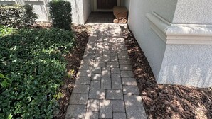 A paved pathway leading to a door, flanked by trimmed bushes and a small bench. - Magical Kingdom of Champions, 6-bed pool home golfing resort close to Disney! (Davenport)