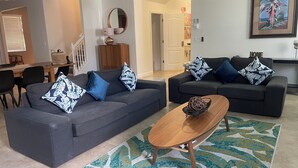 A modern living room with two dark grey sofas, each adorned with patterned pillows, a wooden coffee table, and a patterned rug. - Magical Kingdom of Champions, 6-bed pool home golfing resort close to Disney! (Davenport)