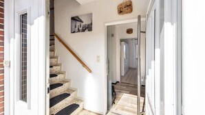 Una escalera con barandilla de madera, un escalón con alfombra negra y beige, y una puerta blanca con panel de vidrio.