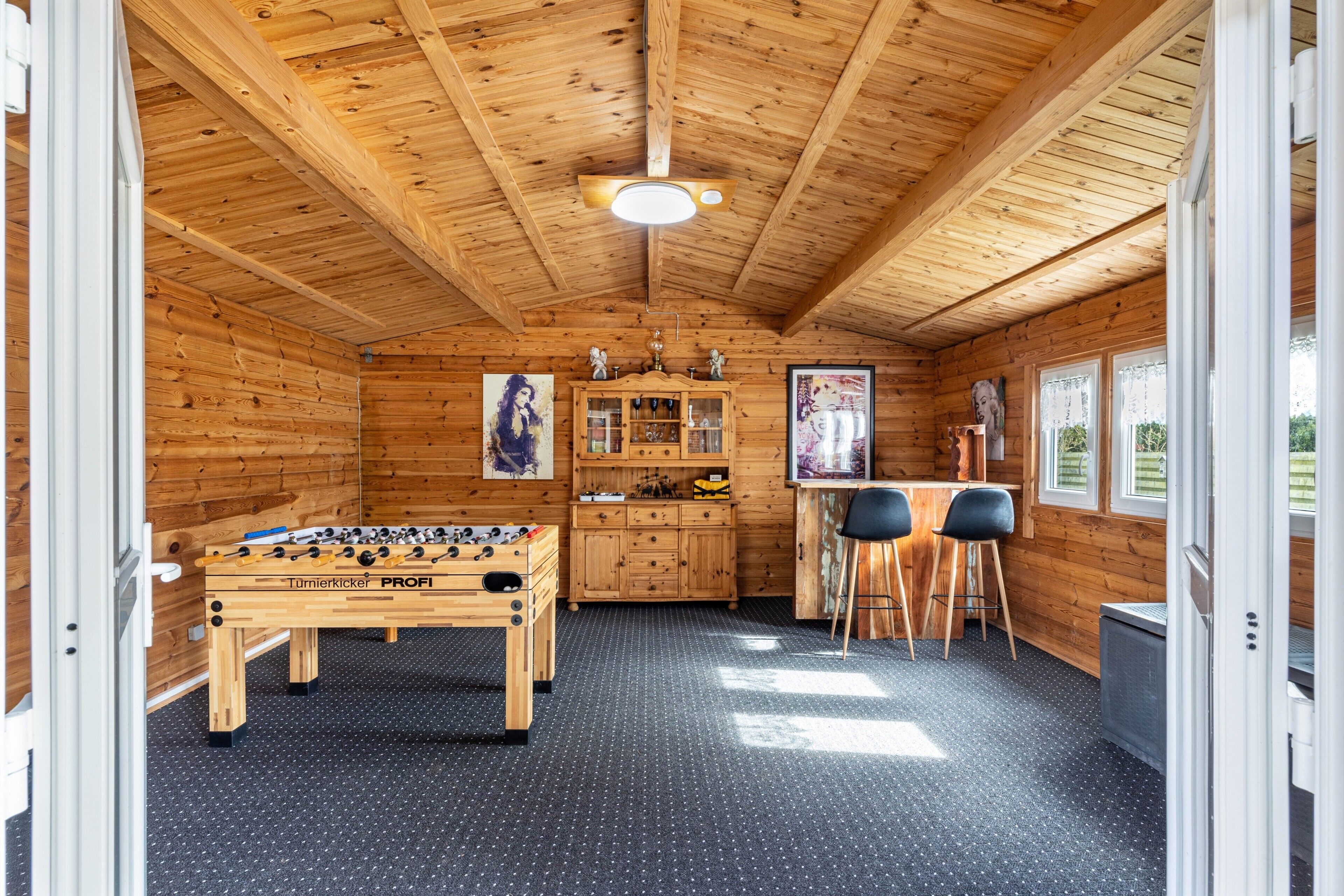 A wooden interior with a foosball table, a cabinet, and two bar stools.