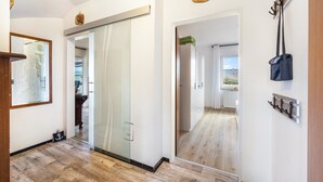 Un pasillo con puerta de vidrio, suelo de madera, perchero y un cuadro en la pared.
