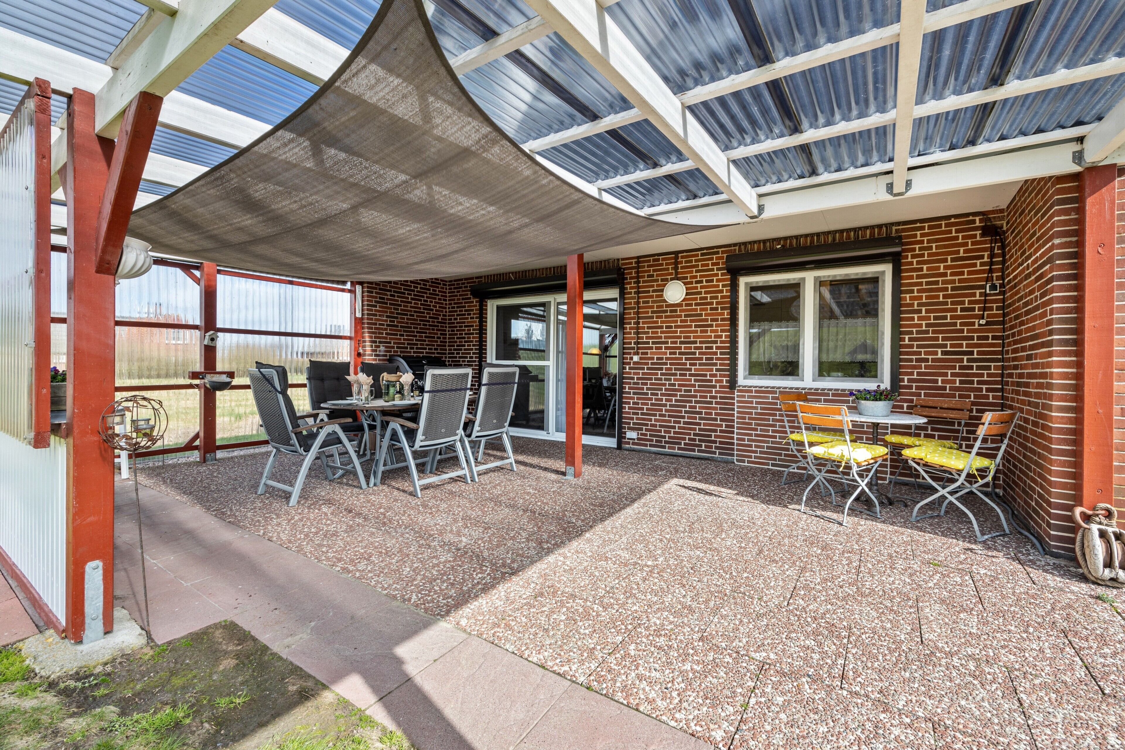 Un patio couvert avec une table et des chaises, un bâtiment en briques et une structure de toit en verre.