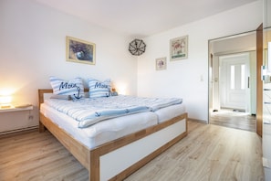Une chambre à coucher avec un lit en bois, des murs blancs et une porte qui donne sur une autre pièce.