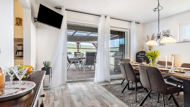 Un comedor con una mesa dispuesta para cuatro personas, un televisor montado en la pared y vistas del patio exterior.