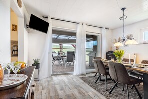 Un coin repas avec une table dressée pour quatre personnes, un téléviseur fixé au mur et une vue sur la terrasse extérieure.
