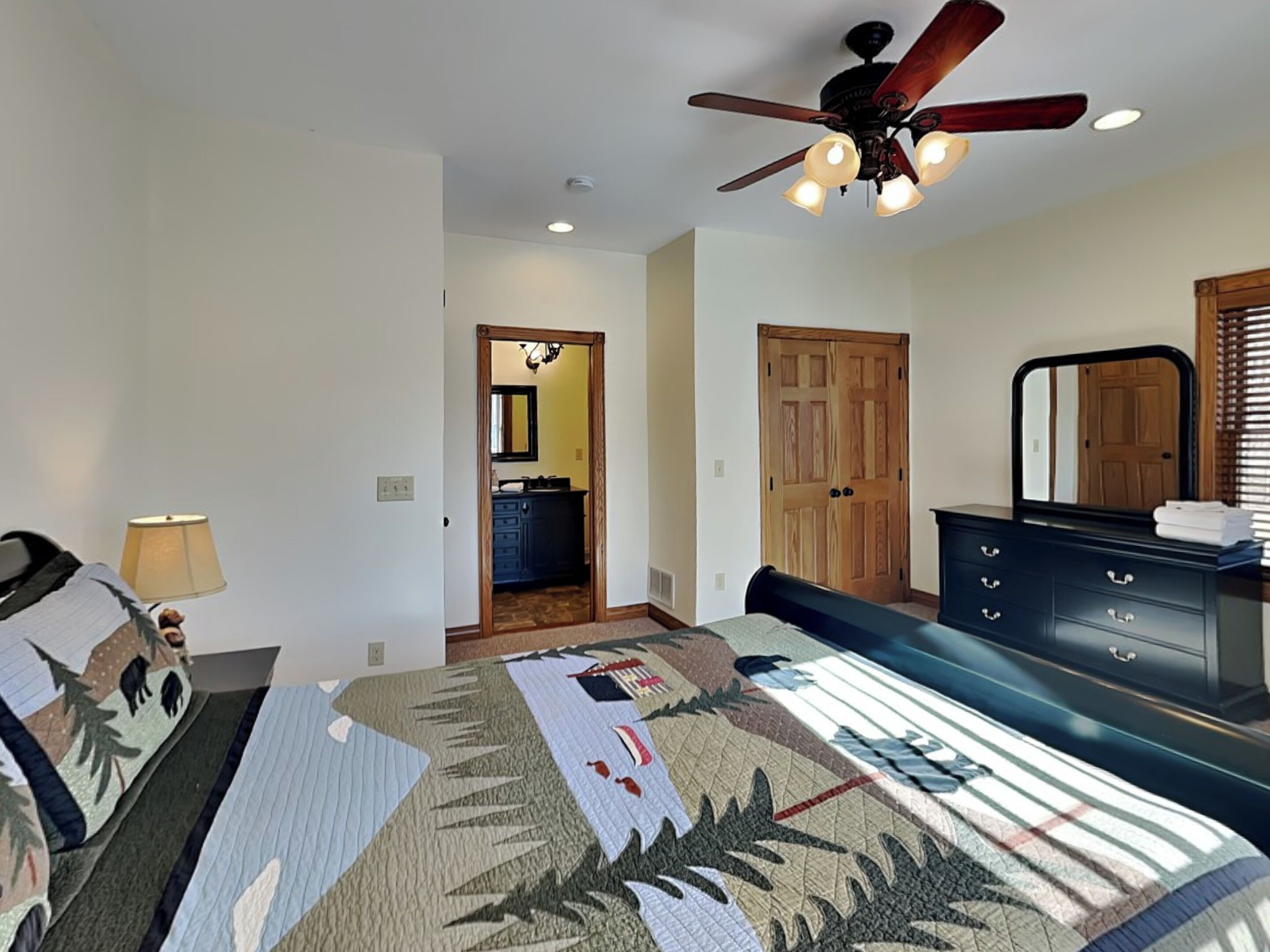 A bedroom with a bed, a dresser, a ceiling fan, and a door leading to a bathroom.