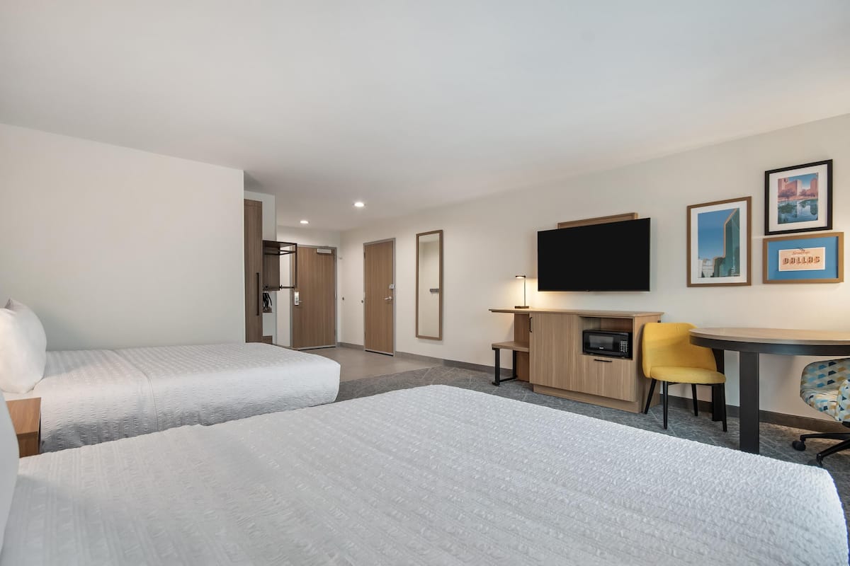 A hotel room with two beds, a desk, a chair, a TV, and framed pictures on the wall.