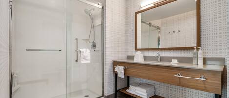 A modern bathroom with a glass shower enclosure, a wooden vanity with a mirror, and a tiled backsplash.