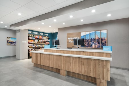A hotel reception area with a wooden reception desk, a cityscape mural, and a snack display.