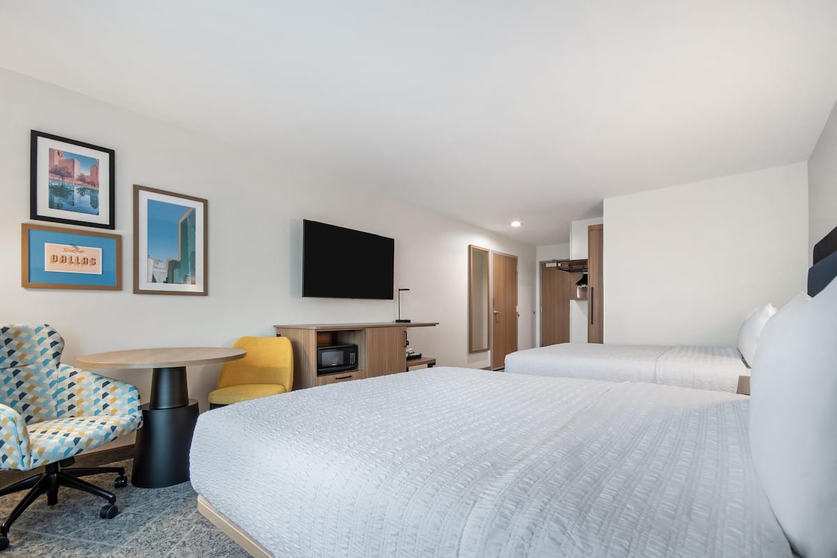 A hotel room with two beds, a desk, a chair, a TV, and framed pictures on the wall.