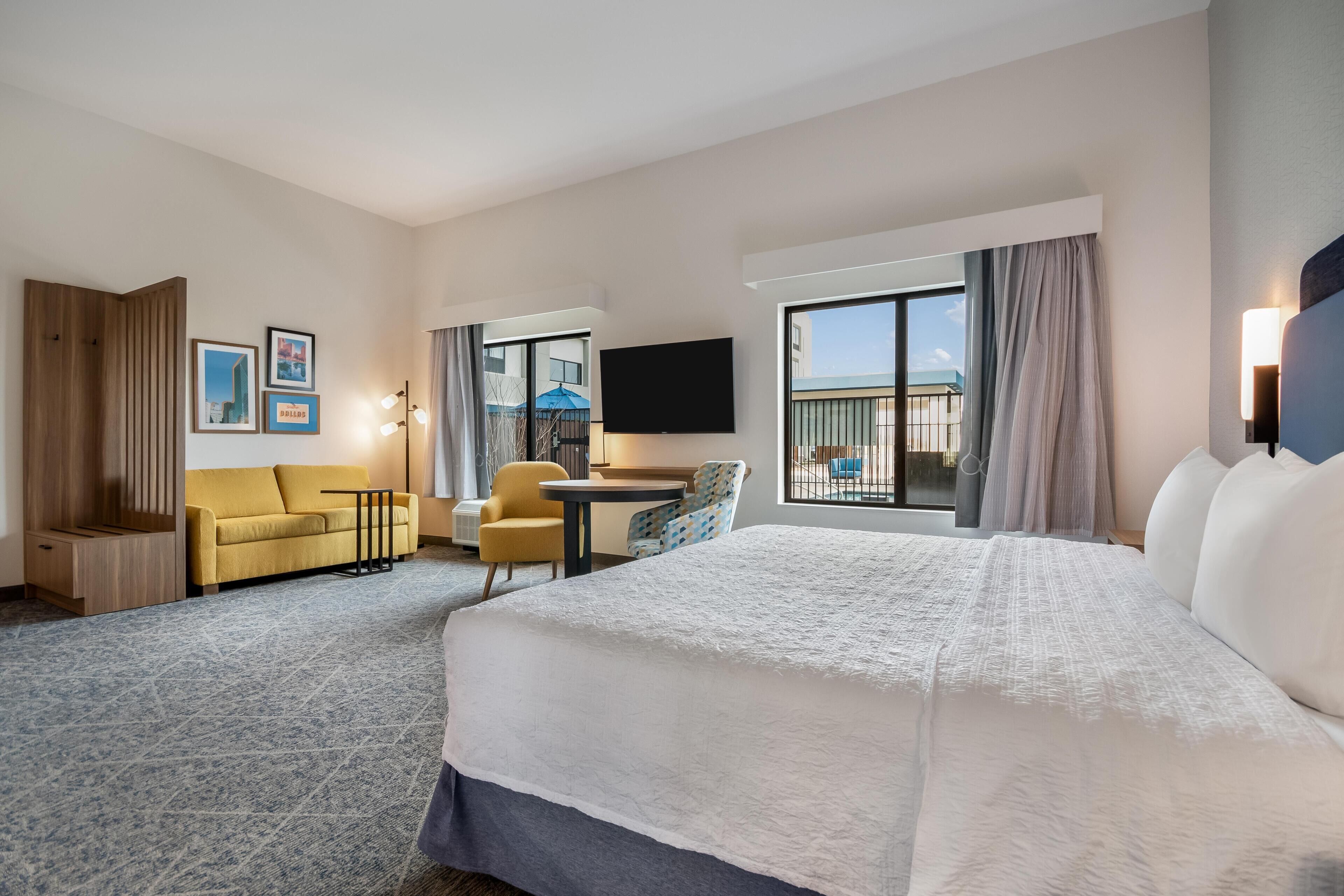 Quarto de hotel com cama, sofá, escrivaninha, cadeira, televisão e varanda com vista.