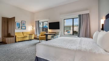 Quarto de hotel com cama, sofá, escrivaninha, cadeira, televisão e varanda com vista.