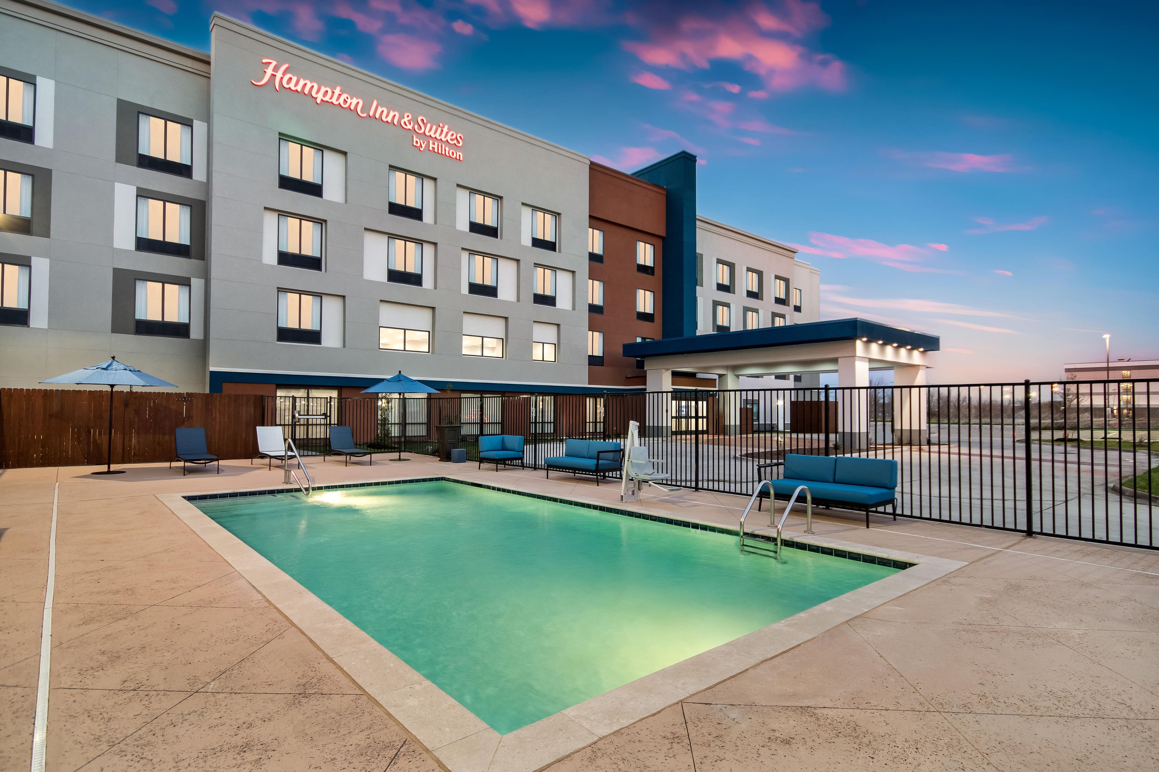 Un hotel con piscina, mobiliario exterior y cielo despejado.