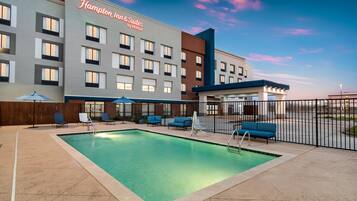 Un hotel con piscina, mobiliario exterior y cielo despejado.