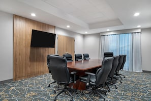 A conference room with a wooden panel wall, a flat-screen TV, a large conference table, and black leather chairs.