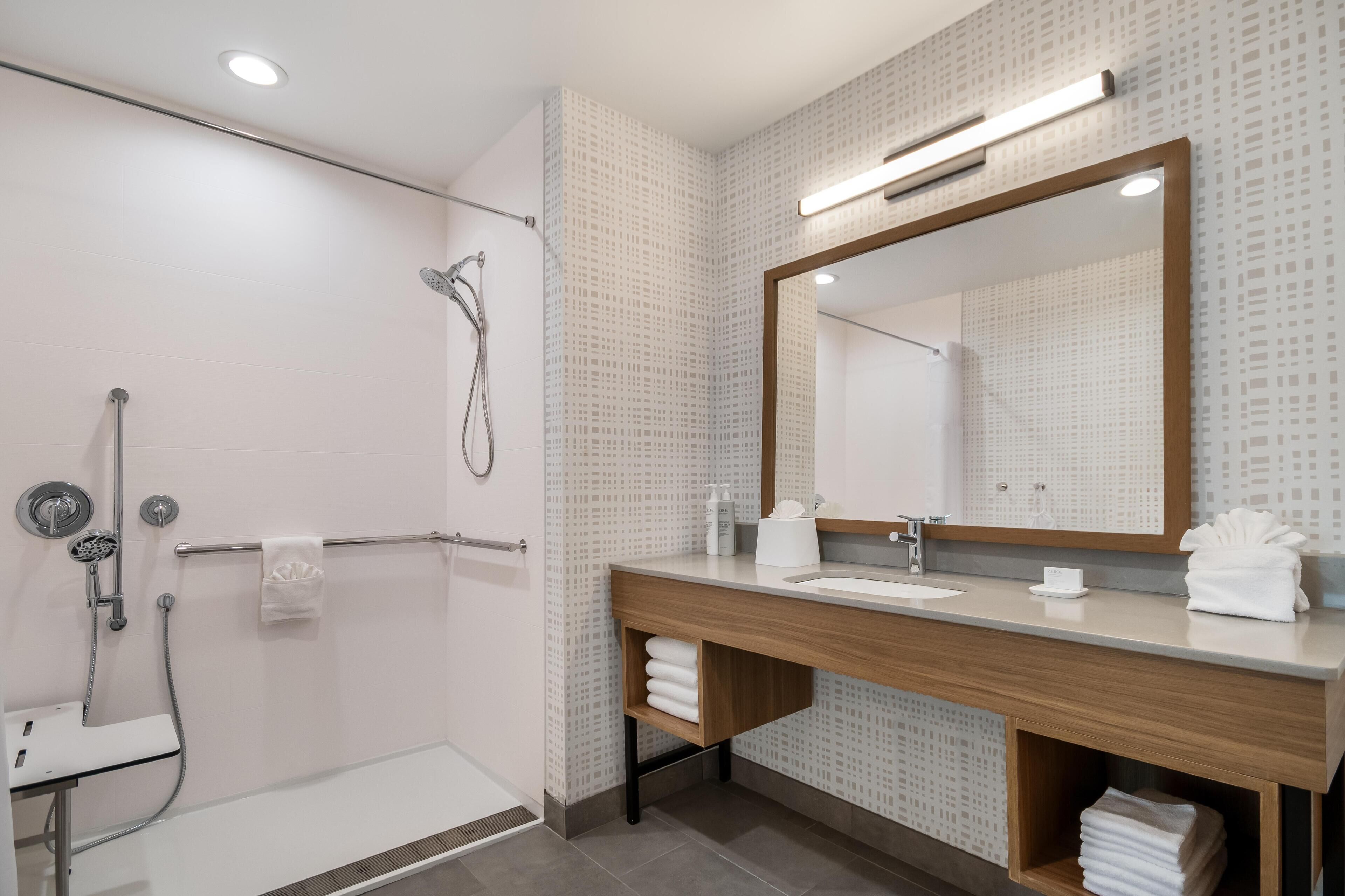 Une salle de bain moderne équipée d’une douche, d’un meuble-lavabo avec miroir et d’un porte-serviettes.
