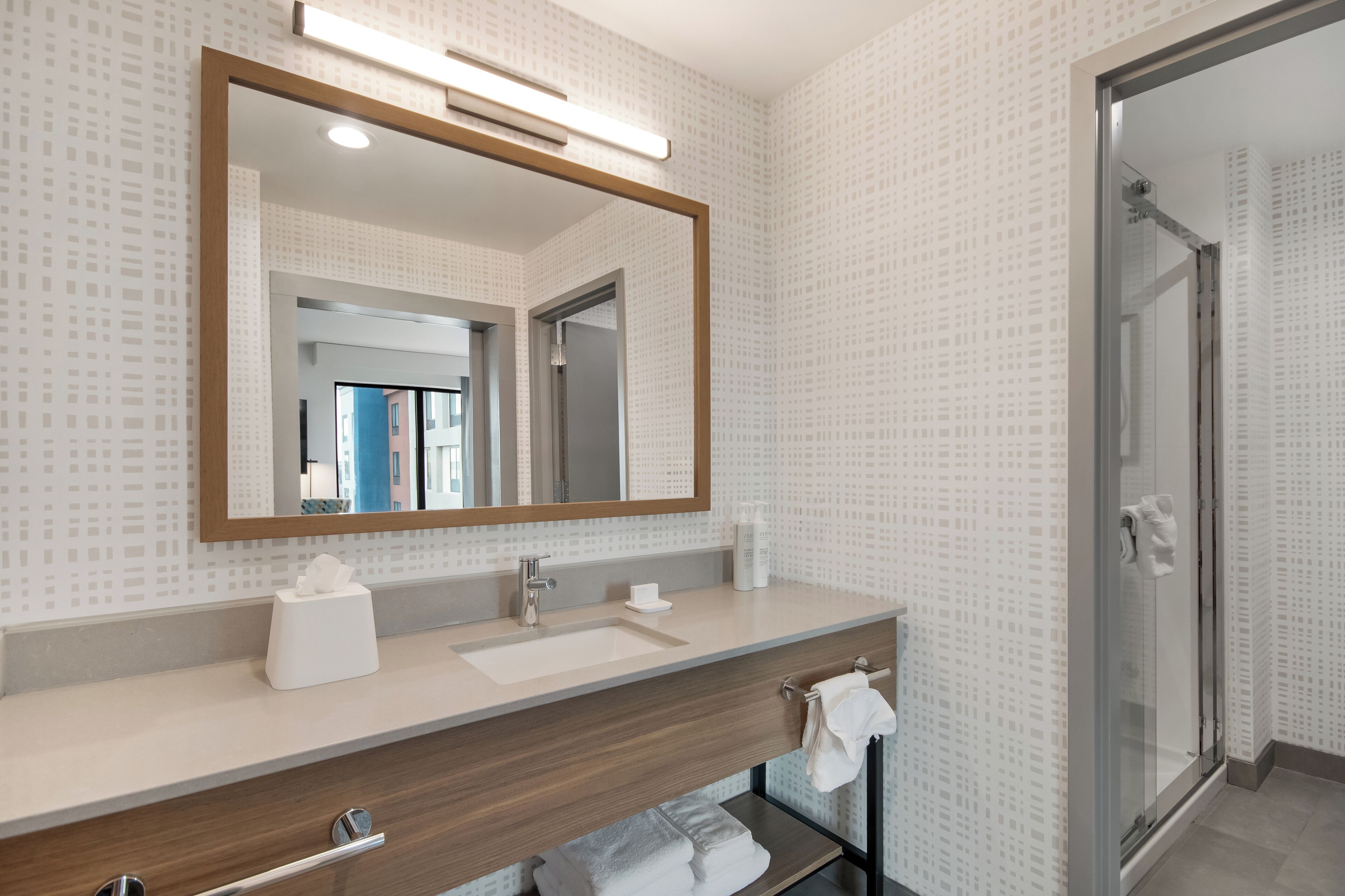 A modern bathroom with a large mirror, a sink, a shower, and a towel rack.