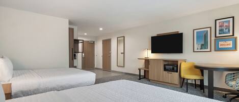 A hotel room with two beds, a desk with a chair, a television, and framed pictures on the wall.