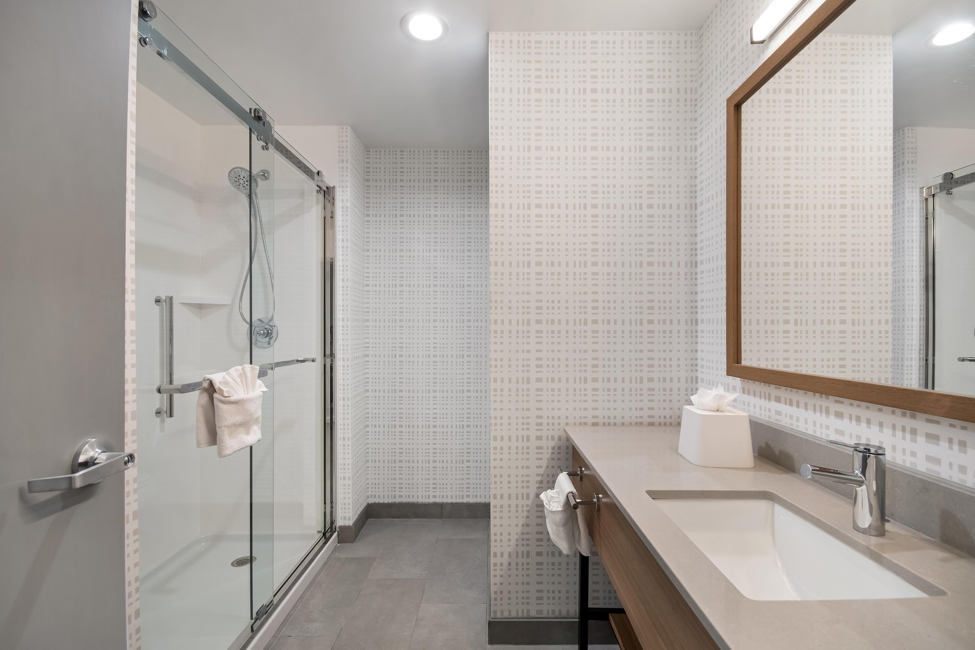 A modern bathroom with a glass shower enclosure, a sink with a mirror, and patterned wall tiles.