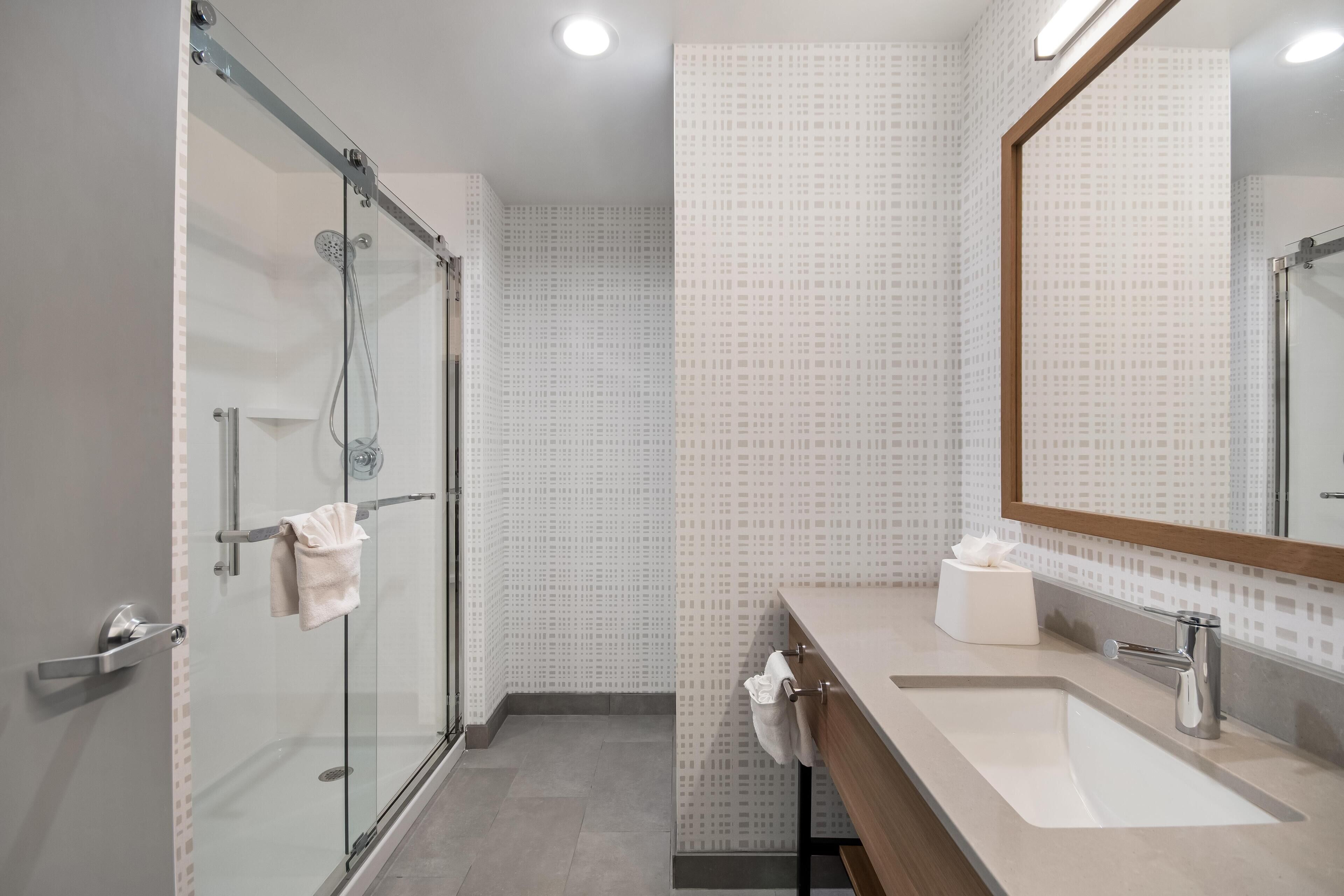 A modern bathroom with a glass shower enclosure, a sink with a mirror, and patterned wall tiles.