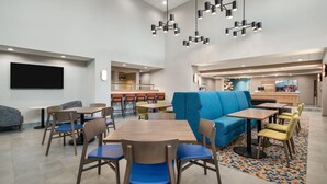 Een moderne eetruimte met tafels, stoelen, een blauwe bank en een keuken op de achtergrond.