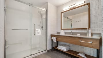A modern bathroom with a glass shower enclosure, a wooden vanity with a mirror, and a tiled floor.