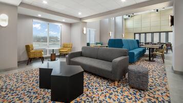 A modern lounge area with a grey sofa, yellow patterned chairs, a blue sofa, and a patterned rug.