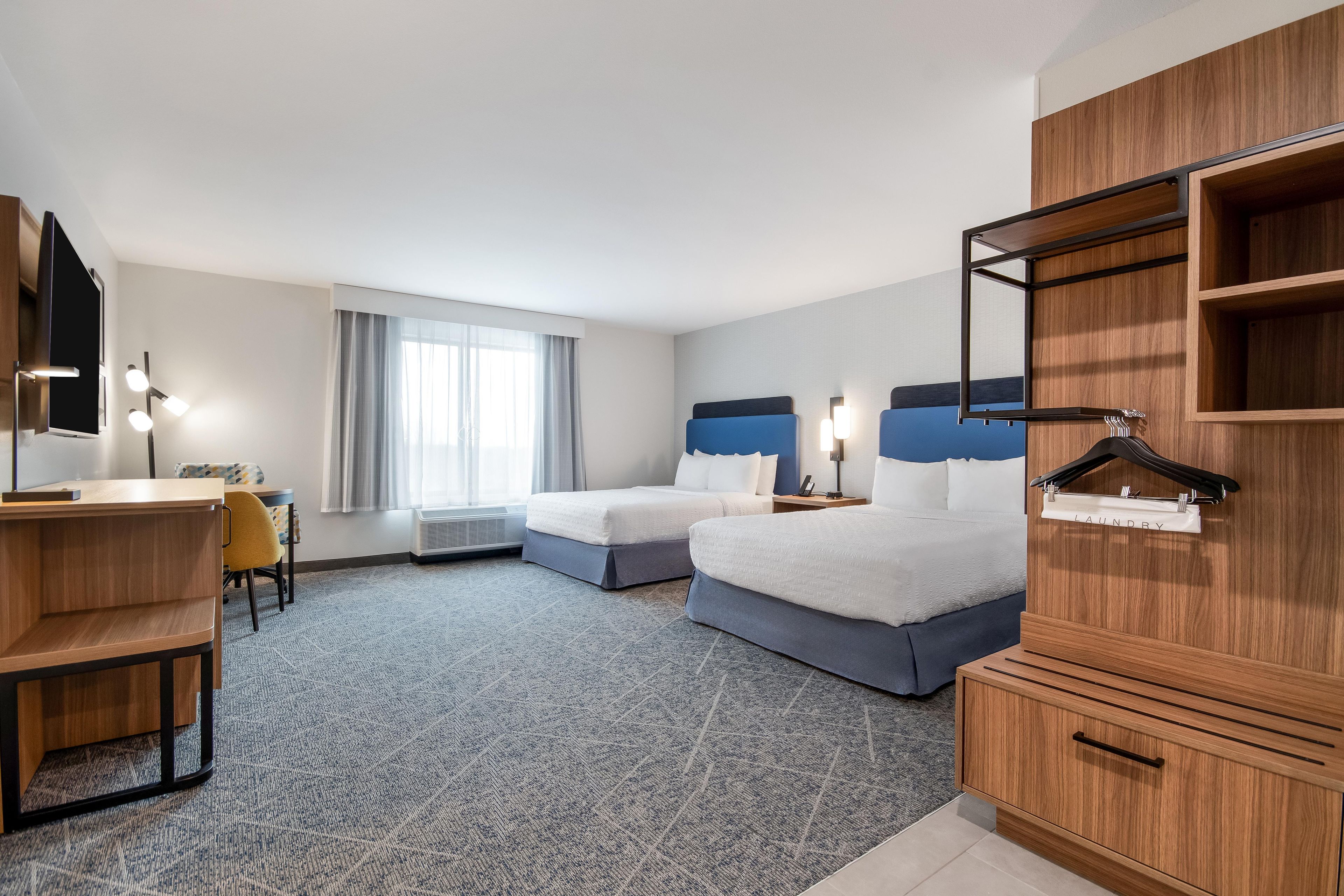 Une chambre d’hôtel avec deux lits, un bureau, une chaise, une armoire et une fenêtre avec des rideaux.