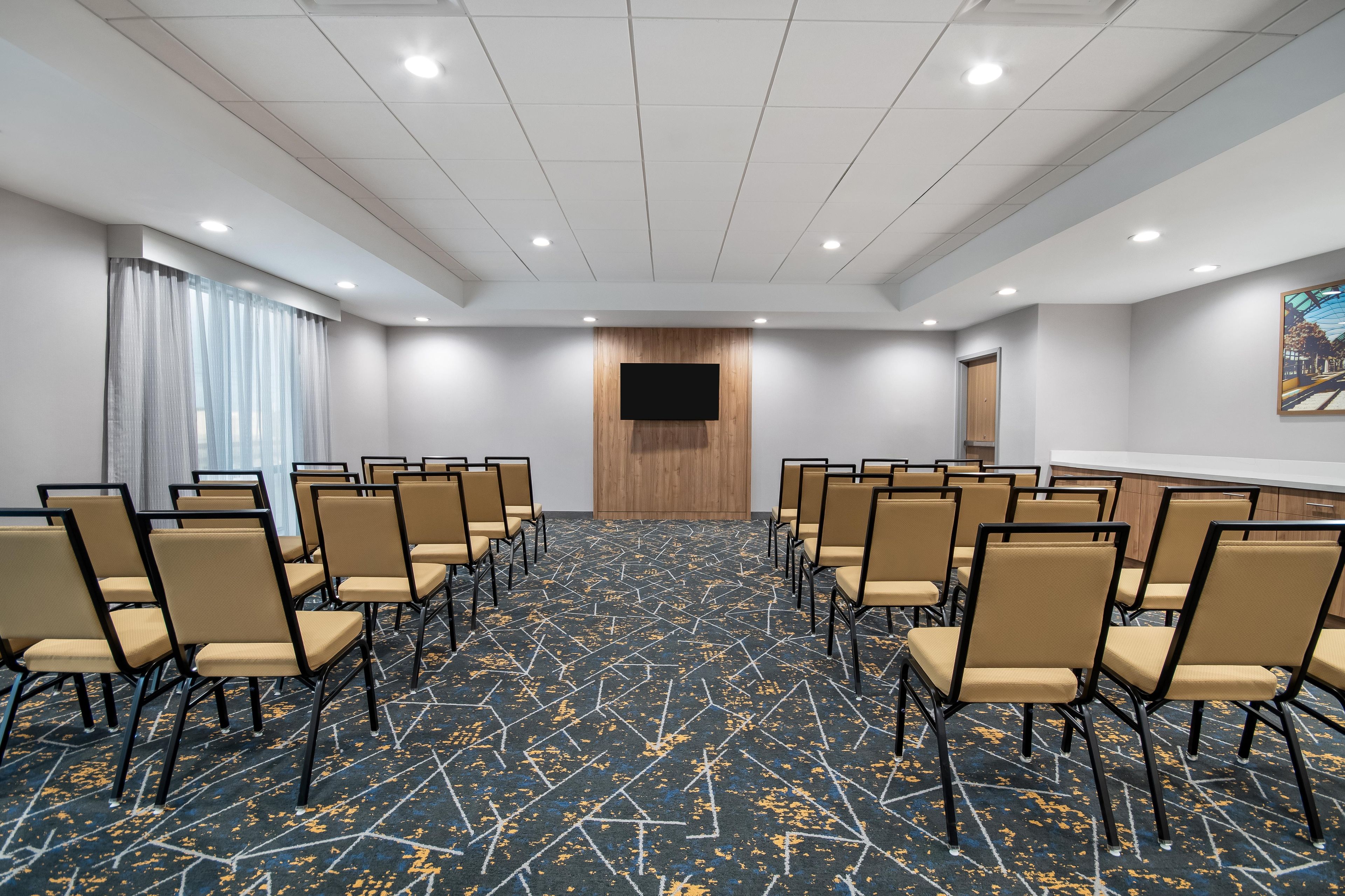 A conference room with rows of chairs, a large screen, and a patterned carpet.