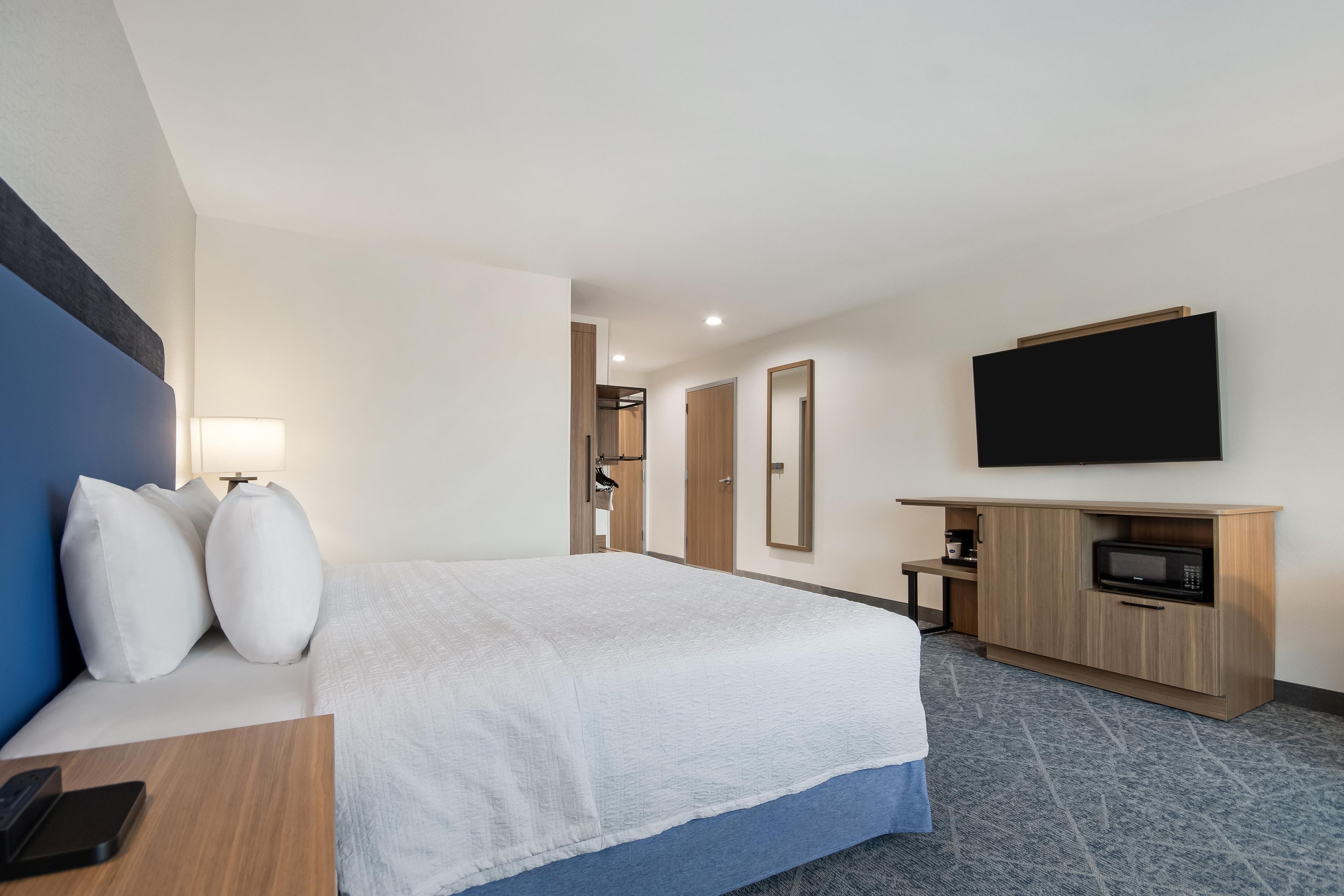 A hotel room with a bed, a TV, a microwave, and a desk with a phone.