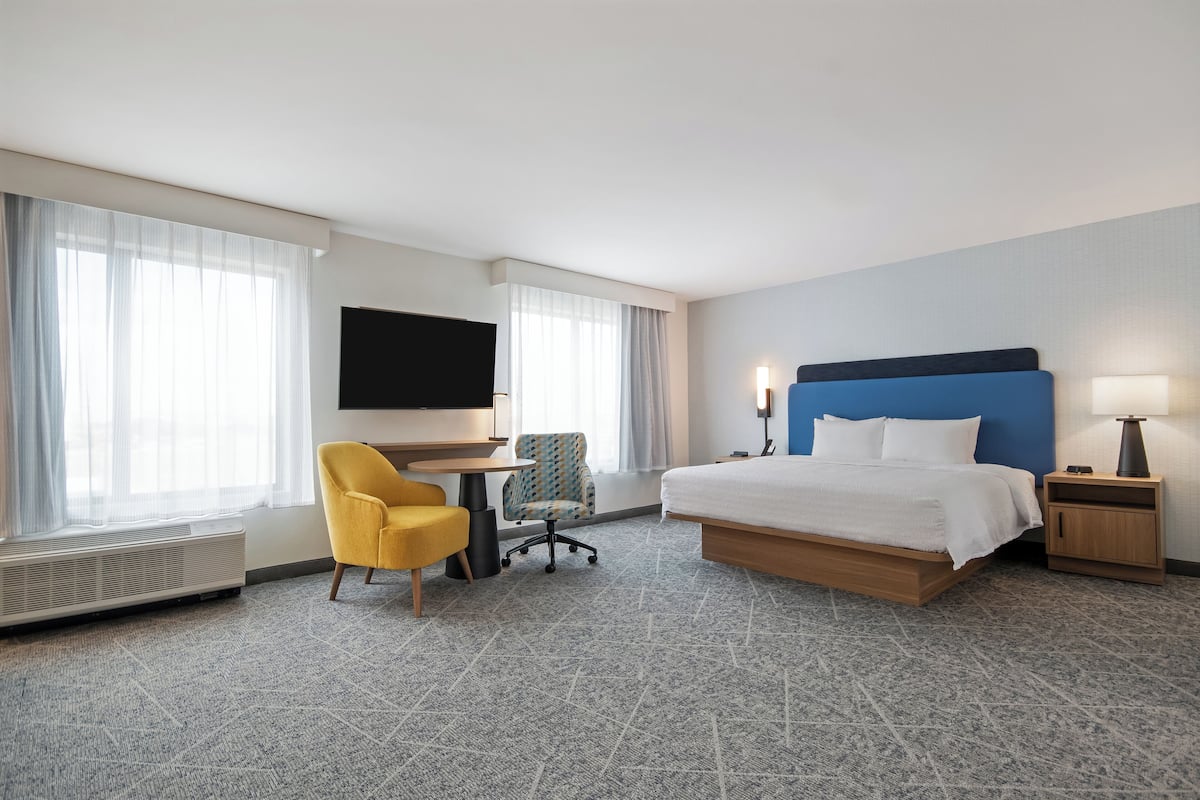 A hotel room with a bed, a desk, a chair, a TV, and a lamp.