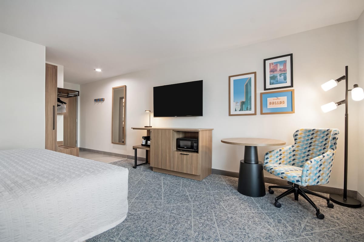 A hotel room with a bed, a TV, a microwave, a chair, and a small table.