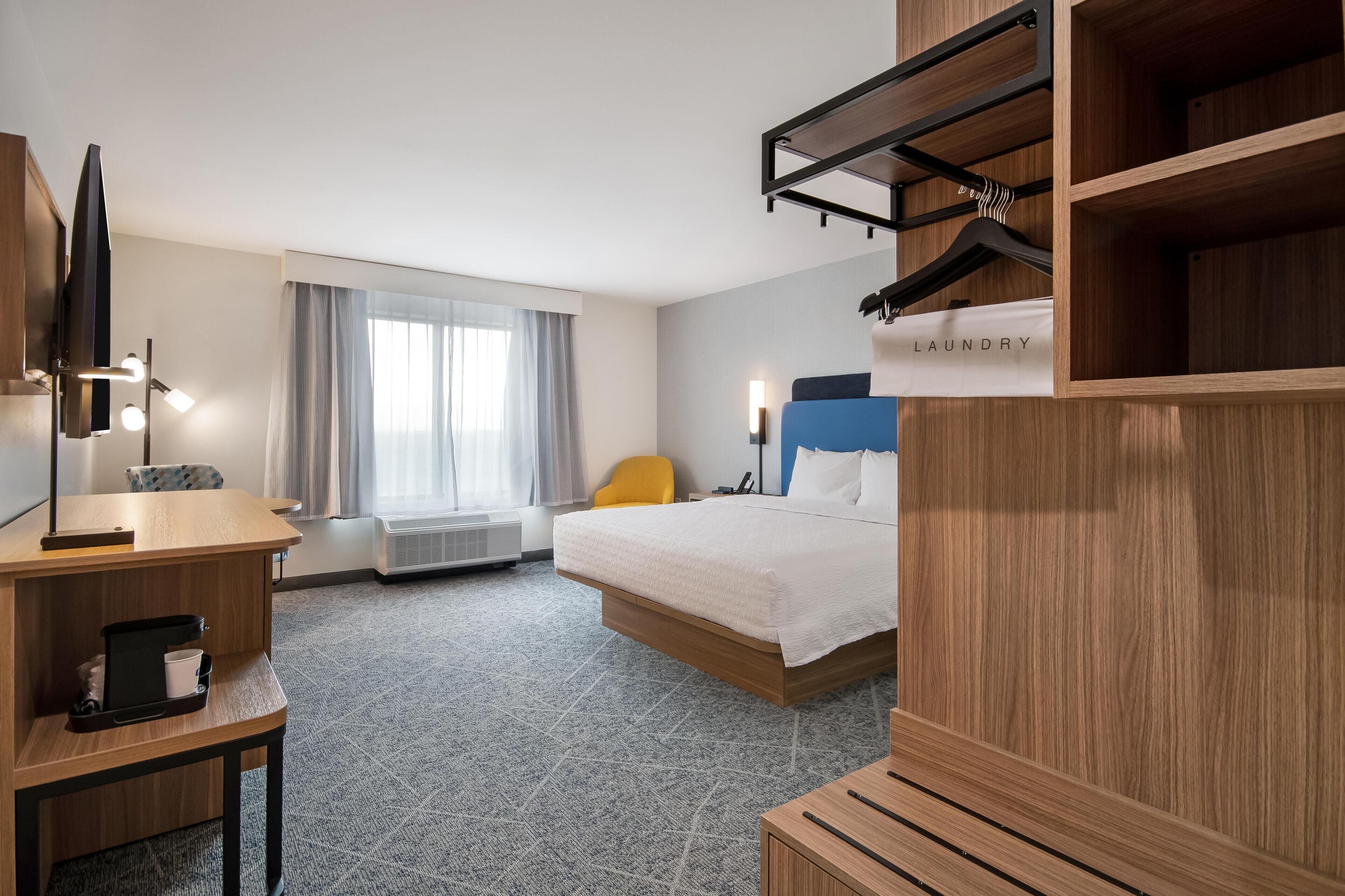 Habitación de hotel con cama, escritorio, silla, televisión, armario y letrero de lavandería.