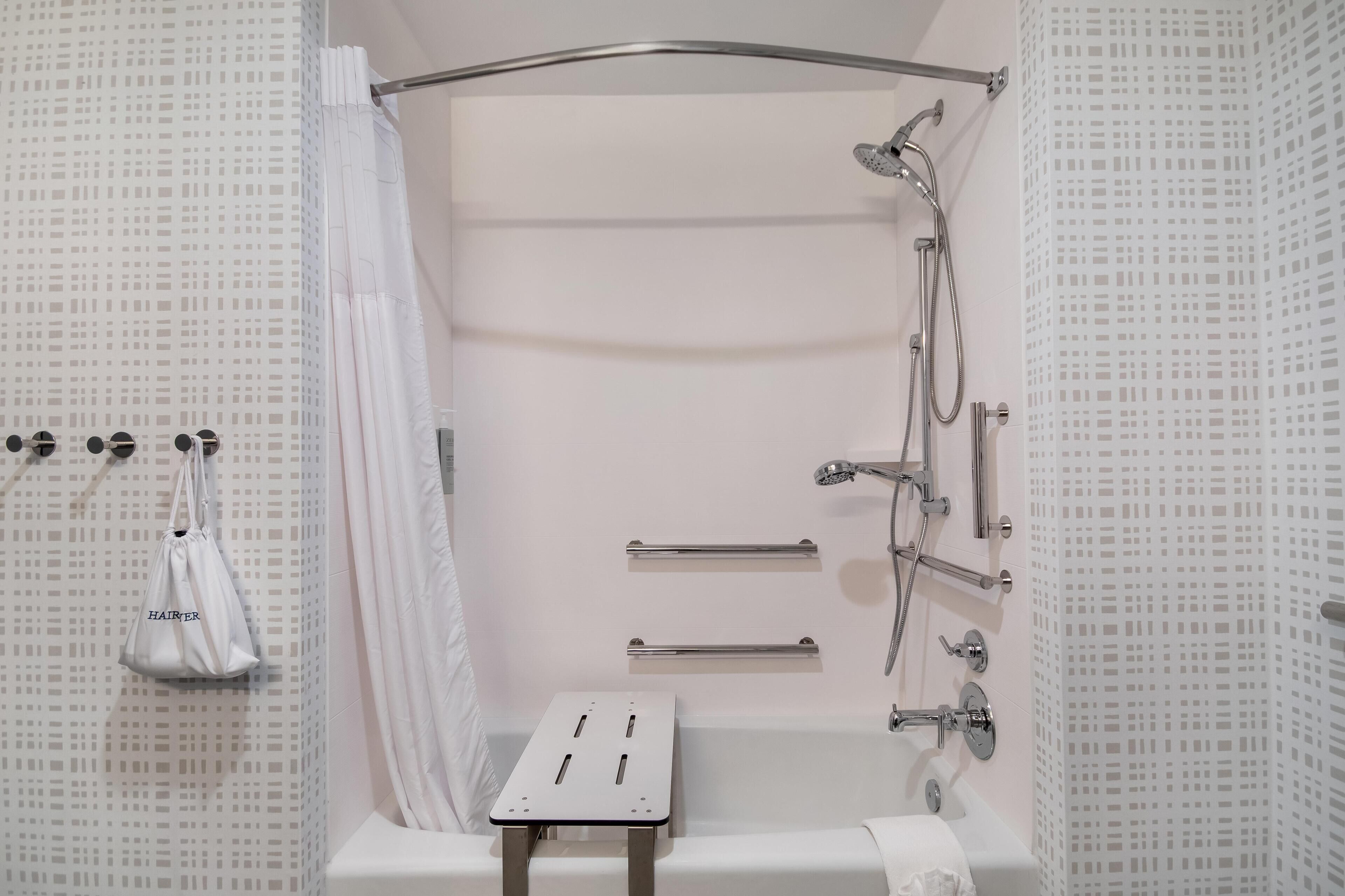 A modern bathroom with a shower, grab bars, and a towel rack.