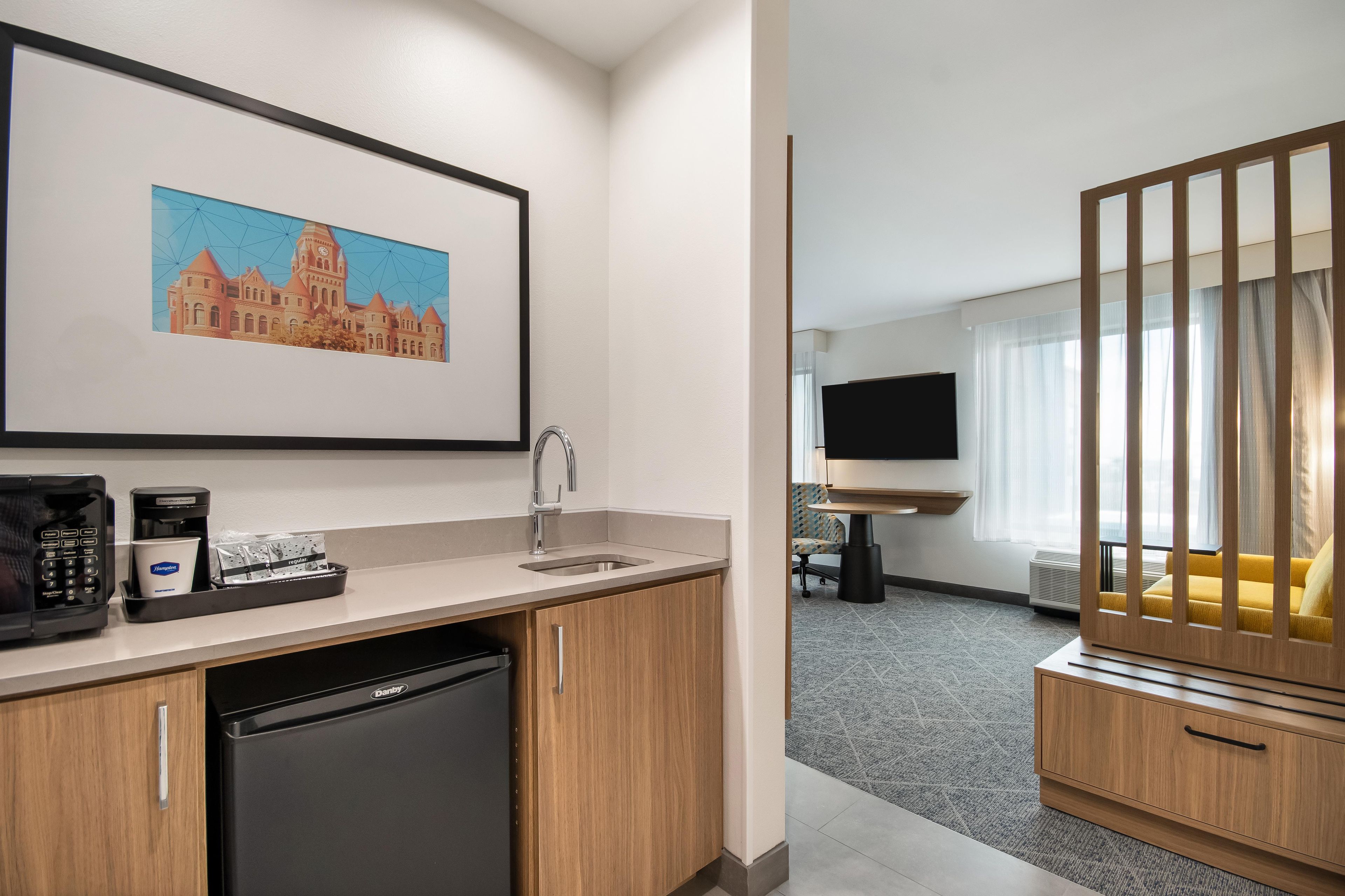 A hotel room with a kitchenette, a flat-screen TV, a sofa, and a framed picture on the wall.