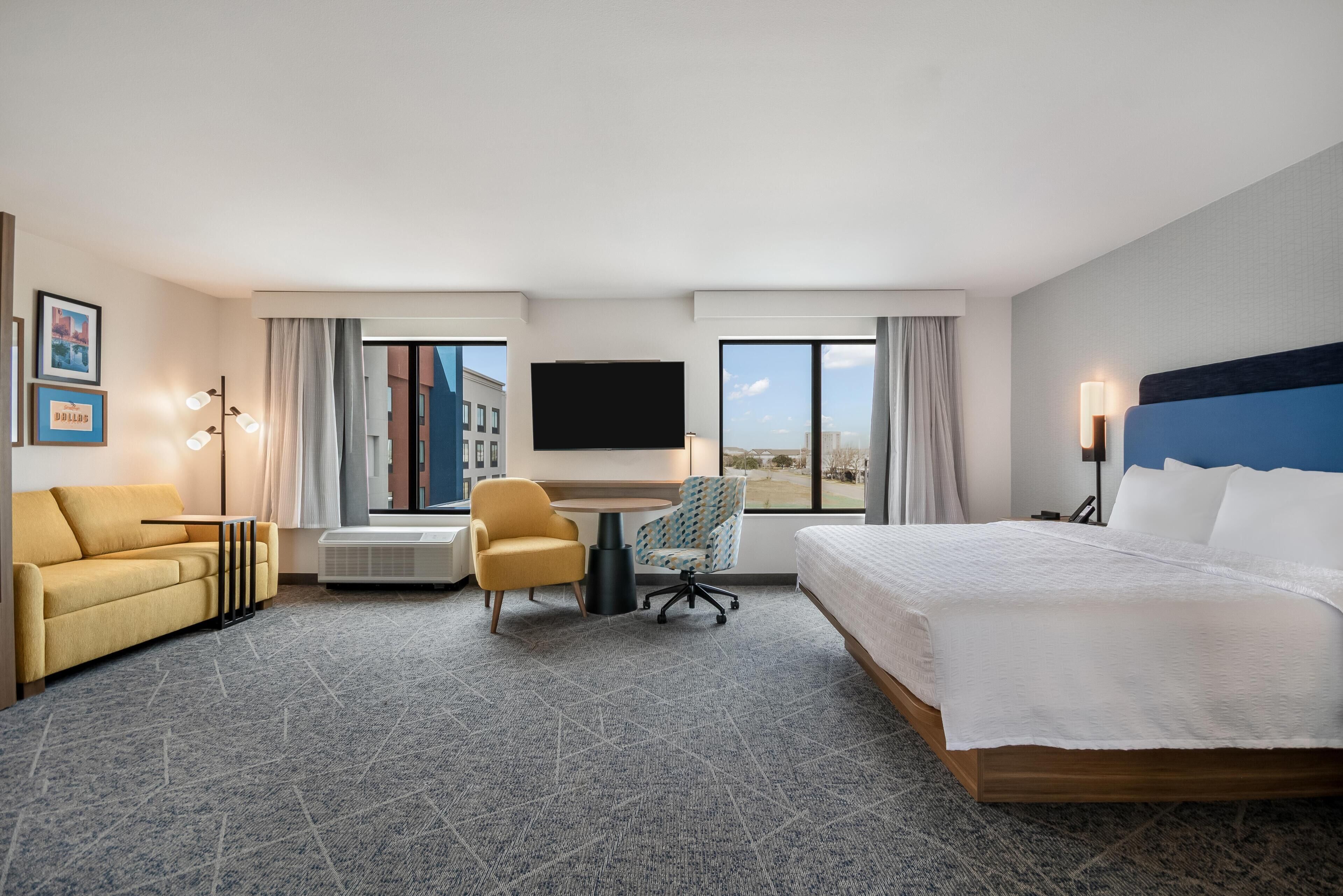 A hotel room with a bed, a desk, a chair, a TV, and a view of the city.