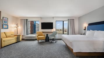 A hotel room with a bed, a desk, a chair, a TV, and a view of the city.