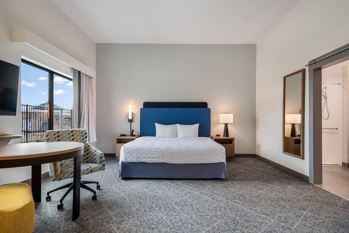 A hotel room with a bed, a desk, a chair, a TV, a window, and a bathroom door.
