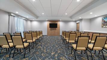 A conference room with rows of chairs, a large screen, and a patterned carpet.