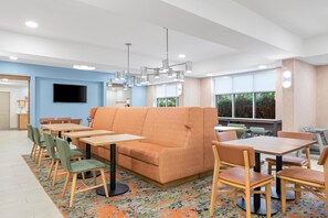 A modern dining area with a sofa, tables, chairs, and a television. - Hampton Inn Midland West (Midland)