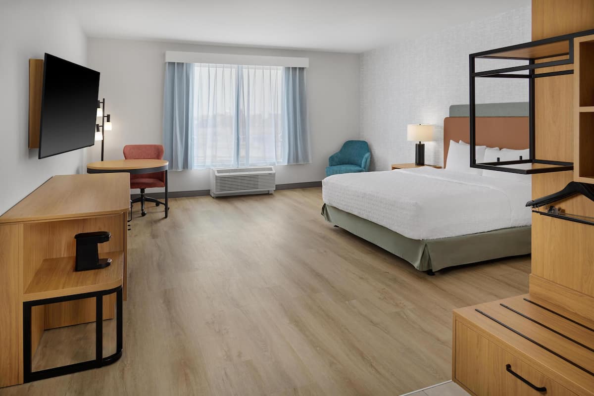 A hotel room with a bed, desk, chair, TV, and a window with curtains.