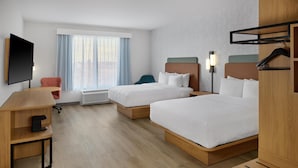 Habitación de hotel con dos camas, un escritorio, una silla, un televisor y una ventana con cortinas.