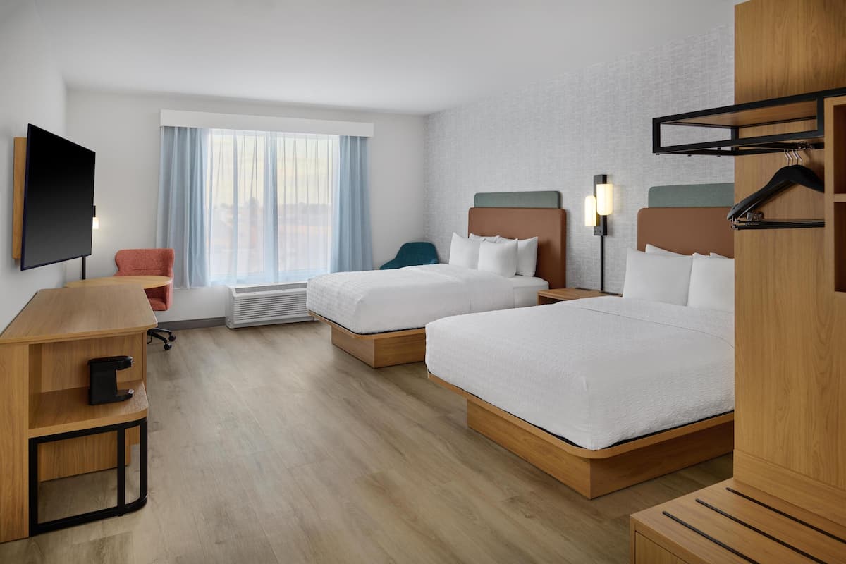 A hotel room with two beds, a desk, a chair, a TV, and a window with curtains.
