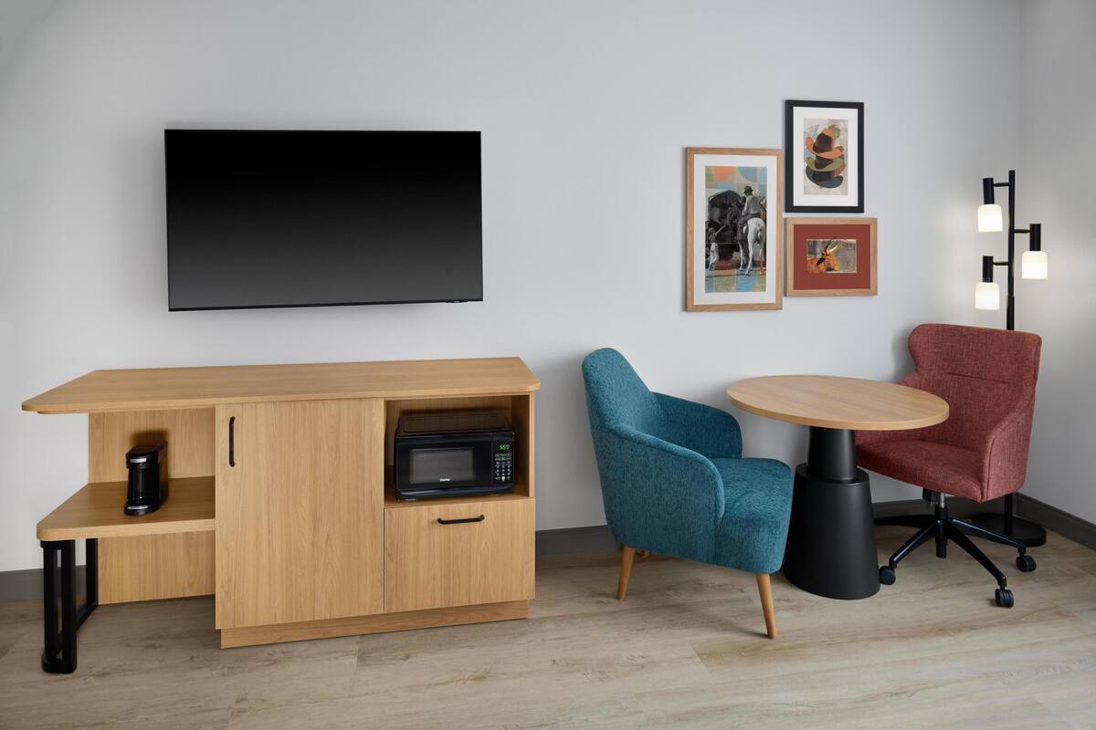A modern room with a wooden desk, a flat-screen TV, a small table, two chairs, and framed pictures on the wall.