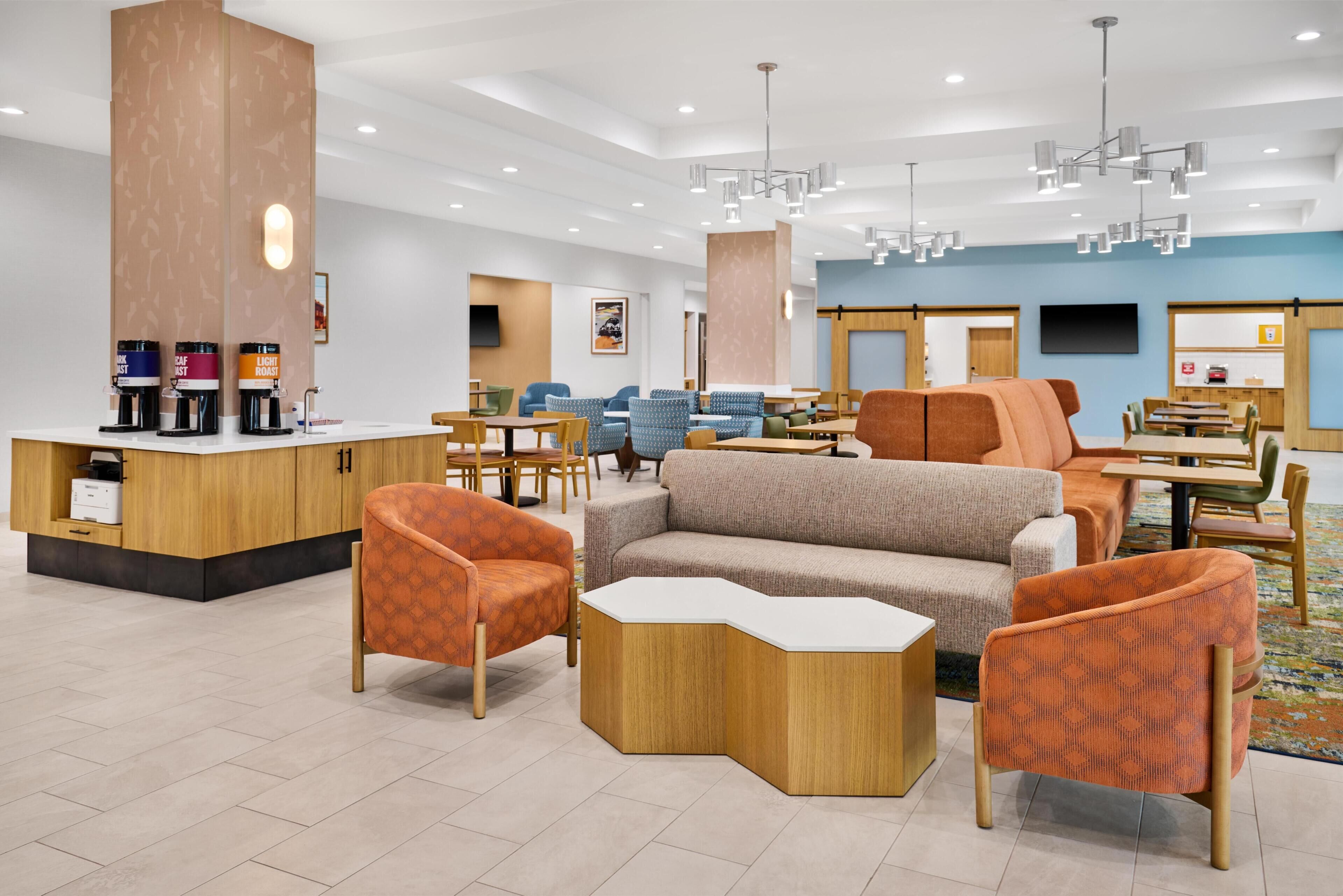 A modern hotel lobby with a reception desk, seating area, and a large flat-screen TV.