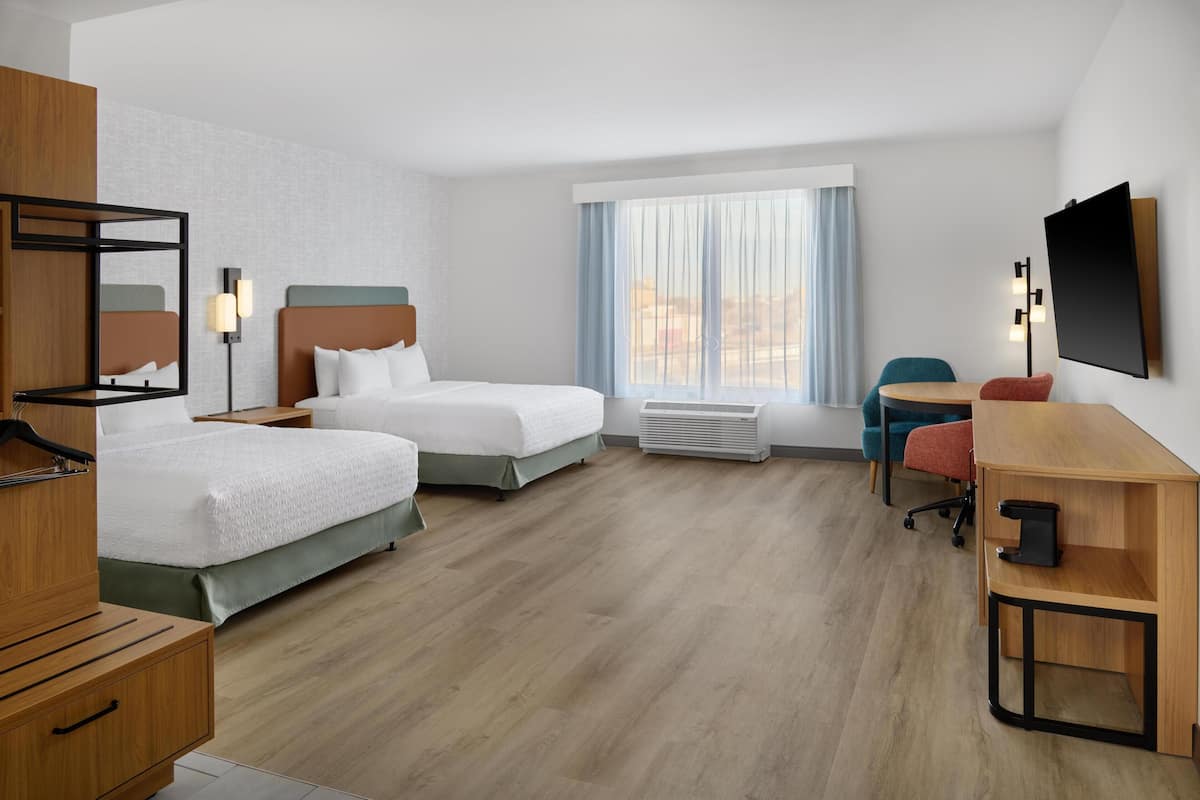 A hotel room with two beds, a desk, a chair, a TV, and a window with curtains.