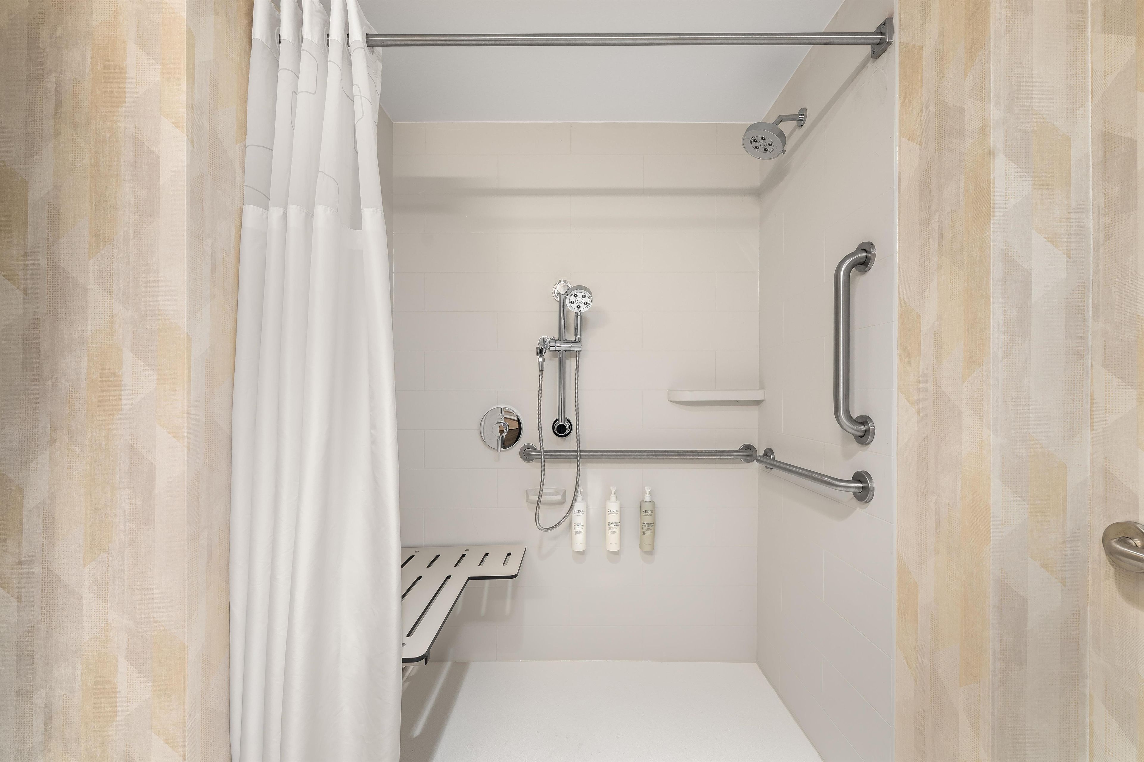 Baño con ducha, barras de apoyo, inodoro y lavabo.