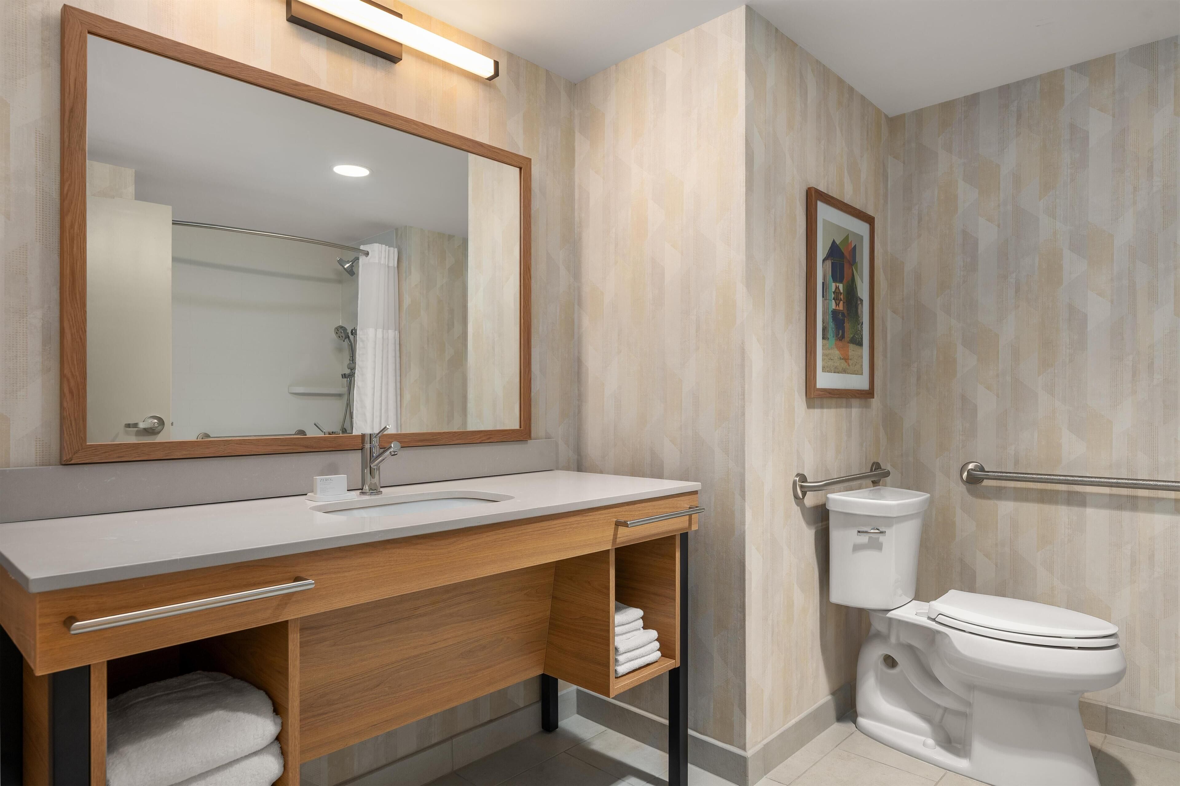 A modern bathroom with a wooden vanity, a large mirror, a toilet, and a shower area.